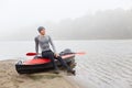 Happy smiling satisfied man having rest after padding, sitting on his boat and looking in distance, keeps his palm on his knee,