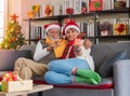 Smiling Senior Caucasian couple wearing Santa hat sitting together on sofa couch holding Christmas gift at home with decorated Royalty Free Stock Photo