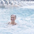 Happy smiling senior caucasian woman in outdoor thermal swimming pool. On background water cannons