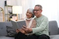 Happy smiling senior family couple in love reading book together, hugging embracing while spending free time at home on retirement Royalty Free Stock Photo