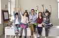 Happy smiling teacher and student with raised hands up sitting on classroom desk