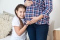 Happy and smiling teen age daughter listen belly of pregnant mother, touching with hand