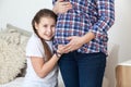 Happy and smiling teen age daughter listen belly of pregnant mother, touching with hands
