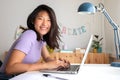 Happy, smiling teen asian female college student studying at home, doing homework using laptop looking at camera. Royalty Free Stock Photo