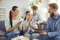 Happy girl in party hat celebrating birthday with family at home, looking at cake with candles Royalty Free Stock Photo