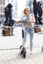 Happy Smiling teenager blonde girl with electric kick scooter on a beautiful day in a European city. Lifestyle portrait Royalty Free Stock Photo