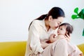 Happy smiling toddle baby sitting on mother lap on yellow sofa in living room at home, mom kissing her little girl daughter, Royalty Free Stock Photo