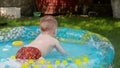 Happy smiling toddler boy playing in inflatable swimming pool on grass at garden