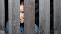 Happy smiling white boy looks out of the crack of a wooden fence. Childish curiosity. Espionage. Rural life. Child Royalty Free Stock Photo