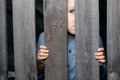 Happy smiling white boy looks out of the crack of a wooden fence. Childish curiosity. Espionage. Rural life. Child Royalty Free Stock Photo