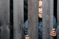 Happy smiling white boy looks out of the crack of a wooden fence. Childish curiosity. Espionage. Rural life. Child Royalty Free Stock Photo