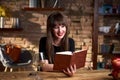 Happy smiling white woman reading book at home in the living room, drinking wine. Warm colors Royalty Free Stock Photo