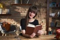 Happy smiling white woman reading book at home in the living room. wearing red glasses, drinking wine. Warm colors Royalty Free Stock Photo