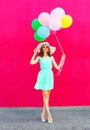 Happy smiling woman with an air colorful balloons is walking over pink background