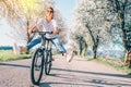 Happy smiling woman cheerfully spreads legs on bicycle on the country road under blossom trees. Spring is comming concept image