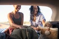 Happy smiling woman freinds put bag and luggage into car trunk