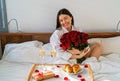 Happy smiling woman holding bouquet of flowers having surprise gift and romantic breakfast in bed on Valentine Day Royalty Free Stock Photo