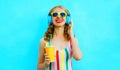 Happy smiling woman holding cup of juice listening to music in wireless headphones on colorful blue Royalty Free Stock Photo