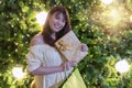 Happy smiling woman holding a golden gift box and shopping bag with lights on Christmas tree background. Happy Royalty Free Stock Photo