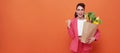 Happy smiling woman holding paper bag full of fresh vegetable groceries pointing her finger isolated on orange copy space Royalty Free Stock Photo