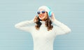 Happy smiling woman listens to music headphones wearing a sunglasses, knitted hat, sweater over blue Royalty Free Stock Photo