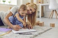 Happy smiling woman mother and baby kid sitting on floor carpet and drawing on paper together Royalty Free Stock Photo