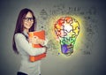 Happy smiling woman with orange folder notebook near a concrete wall with a bright puzzle light bulb business id