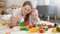 Happy smiling woman playing with her baby boy on carpet and building toy tower with blocks and bricks. Concept of Royalty Free Stock Photo