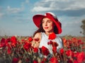 Happy smiling woman in red hat on field of poppies at summer sunset