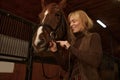 Woman rider putting bridle horsey muzzle while standing in stable Royalty Free Stock Photo