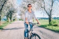 Happy smiling woman rides a bicycle on the country road under blossom trees. Spring is comming concept image