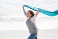 Mature woman running at beach with blue scarf