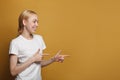 Happy smiling woman seller points at right corner, has friendly facial expression, wears casual white t shirt isolated on yellow Royalty Free Stock Photo