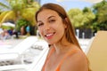 Happy smiling woman sitting on deck chair in tropical pool. Laughing girl enjoying the sun on holidays at hotel resort beach while Royalty Free Stock Photo