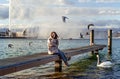 Happy smiling woman sitting on pier on the lake with seagulls and swan enjoying fresh autumn breeze Royalty Free Stock Photo
