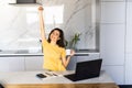 Happy smiling woman sitting at table in kitchen drinking morning coffee reading message looking at device screen using computer Royalty Free Stock Photo