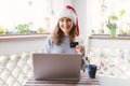 Happy smiling woman sitting at the table with laptop and credit card wearing Santa`s red hat Royalty Free Stock Photo