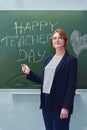 Happy smiling woman standing next to a school blackboard on which teacher`s day greeting is drawn Royalty Free Stock Photo