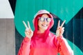 Happy smiling woman in sunglasses with flowers stickers making V sign by fingers. Playful woman with pink hair,bucket