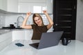 Happy smiling woman with win gesture sitting at table in kitchen drinking morning coffee reading message looking at device screen Royalty Free Stock Photo