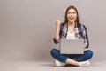 Happy smiling woman working on laptop computer while sitting on the floor with legs crossed and pointing finger away isolated over Royalty Free Stock Photo