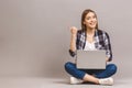 Happy smiling woman working on laptop computer while sitting on the floor with legs crossed and pointing finger away isolated over Royalty Free Stock Photo