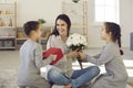 Happy smiling woman mother sitting on floor between her daughters and getting flowers and presents Royalty Free Stock Photo