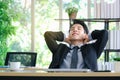 Happy smiling young Asian businessman sitting and relaxing at office working desk, satisfied with work done, happy workplace Royalty Free Stock Photo