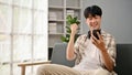 A happy Asian man celebrating his good news while sitting on a sofa in the living room Royalty Free Stock Photo