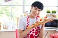 Happy smiling young Asian man in cute red heart apron holding valentine sweet strawberries bread on wooden board, standing behind Royalty Free Stock Photo