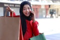 Happy smiling young Asian Muslim women wearing hijab in red dress talking on mobile phone and holding shopping bags on walking Royalty Free Stock Photo