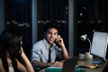 Happy smiling young Asian officer talking with mobile phones at working desk with colleague at night, staff business man work Royalty Free Stock Photo