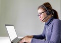 Happy smiling young asian support phone operator in headset with laptop, on grey background with laptop showing white screen