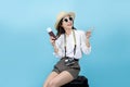 Happy smiling young Asian tourist woman sitting on luggage holding passport and hand pointing to copy space going to travel on Royalty Free Stock Photo